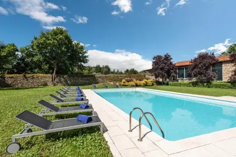 Piscina exterior con tumbonas sobre el césped y muro de piedra en el Áurea Palacio de Sober