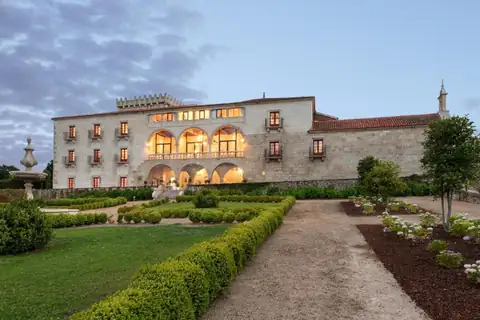 Fachada iluminada del pazo al atardecer con jardines y fuente en el Áurea Palacio de Sober
