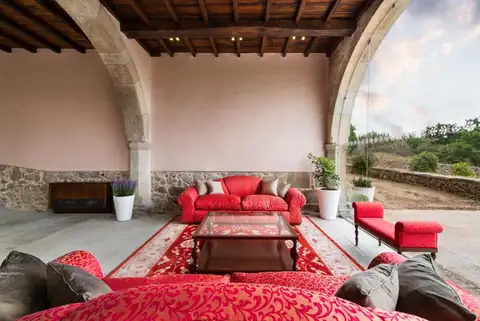 Porche bajo arcos de piedra con sofás rojos abierto al jardín en el Áurea Palacio de Sober