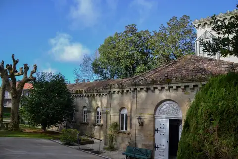 Fachada de piedra con entrada en arco entre árboles del Gran Balneario do Carballiño
