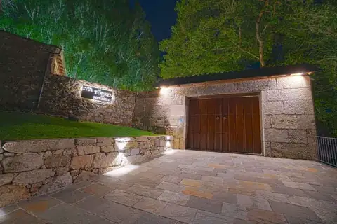 Portalón de madera y muro de piedra iluminados de noche en As Torres da Hermida