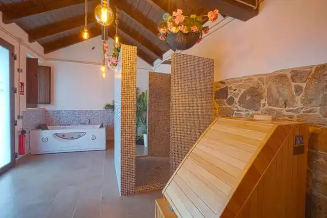 Zona de spa con bañera de hidromasaje, sauna y muros de piedra en As Torres da Hermida