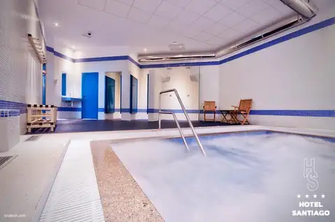 Sala del spa con piscina burbujeante, puertas azules y duchas en el Hotel Auditorio Santiago & Spa