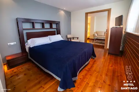 Habitación con cama de matrimonio, colcha azul y suelo de madera en el Hotel Auditorio Santiago