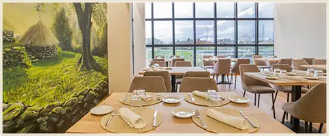 Comedor con mesas preparadas, mural de paisaje y ventanales en el Hotel Auditorio Santiago & Spa