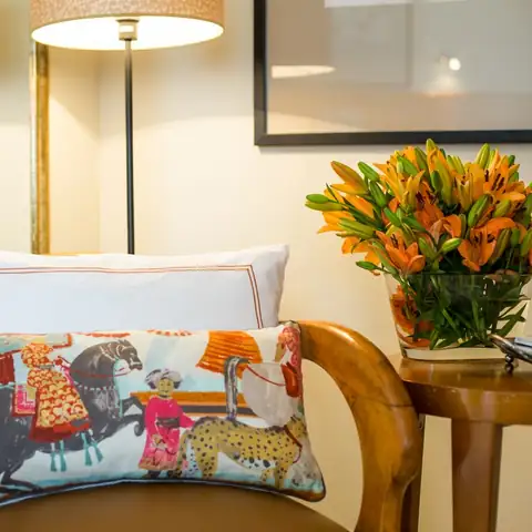 Rincón de habitación con cojín estampado, flores naranjas y lámpara en el Hotel Nuevo Astur & Spa