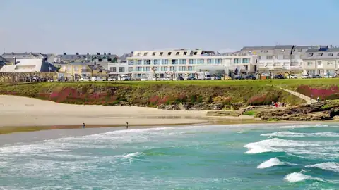 Playa con olas y el edificio blanco del Playa de Foz Hotel & Spa en primera línea