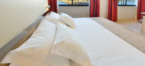 Detalle de cama con almohadas blancas y ventanas a la ría en el Hotel Puente de La Toja