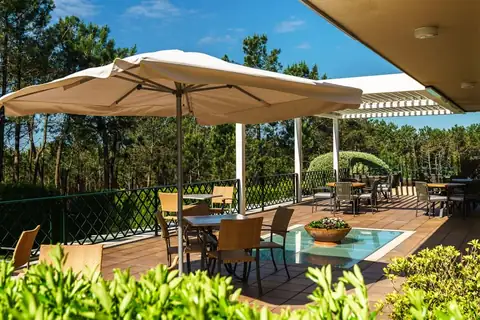 Terraza con sombrilla, mesas y sillas rodeada de vegetación en el Hotel Spa Atlántico de O Grove