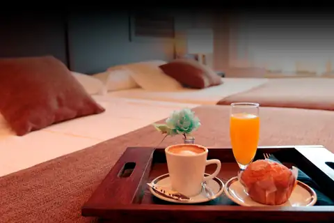 Bandeja de desayuno con café, zumo y magdalena sobre la cama en el Hotel Congreso & Spa