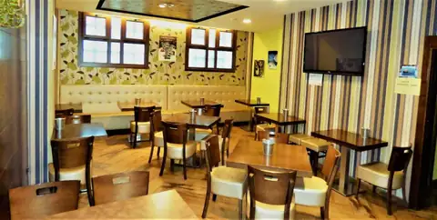 Cafetería con mesas de madera, banco tapizado y televisor en el Hotel Spa Galatea