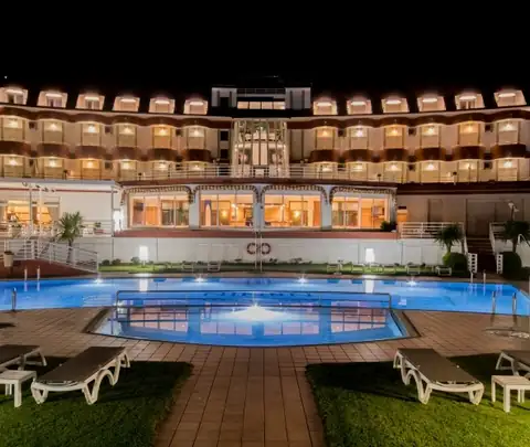 Piscina exterior iluminada de noche ante la fachada del Hotel Spa Nanín Playa