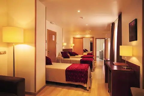 Habitación triple con colchas rojas, escritorio y lámparas de pie en el Hotel Playa Langosteira