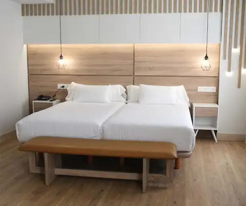 Dos camas con cabecero de madera iluminado y banqueta a los pies en el IMI Hotel & Spa