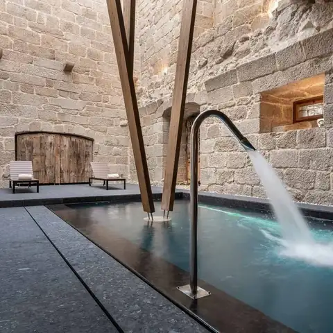 Piscina del spa con chorro de agua entre muros de piedra del antiguo Monasterio de San Clodio