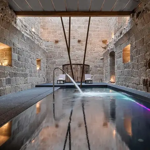 Piscina iluminada bajo vigas de madera y paredes de granito en el spa del Monasterio de San Clodio