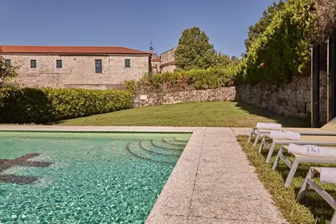 Piscina al aire libre con tumbonas sobre el césped junto a los muros del Monasterio de San Clodio