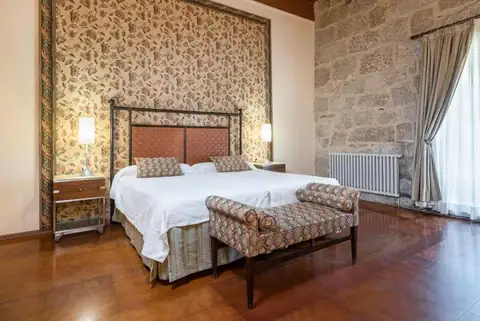 Habitación doble con cabecero tapizado y pared de piedra en el Monasterio de San Clodio