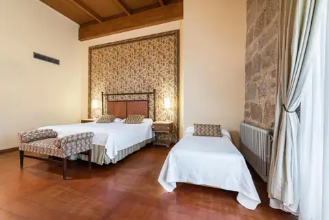 Habitación triple con cama supletoria, techo de madera y piedra vista en el Monasterio de San Clodio