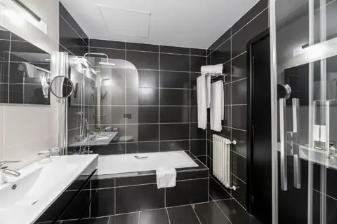 Baño con bañera, ducha acristalada y azulejo negro en una habitación del Monasterio de San Clodio