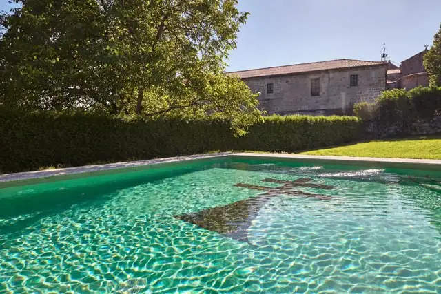 Piscina exterior con una cruz en el fondo y el edificio de piedra del Monasterio de San Clodio