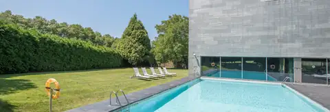Piscina exterior junto al césped y el edificio de pizarra del NH Collection Santiago