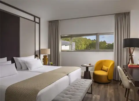 Habitación con dos camas, butaca amarilla y vistas a los árboles en el NH Collection Santiago