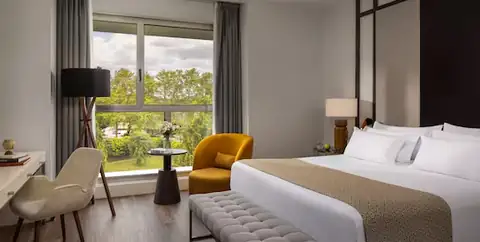 Habitación con cama, butaca amarilla y ventanal al parque en el NH Collection Santiago