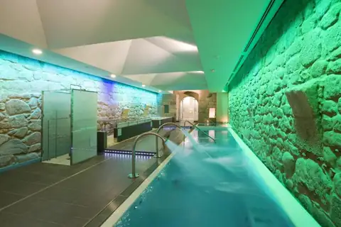 Piscina alargada del spa con muros de piedra iluminados en verde del Parador de Santo Estevo