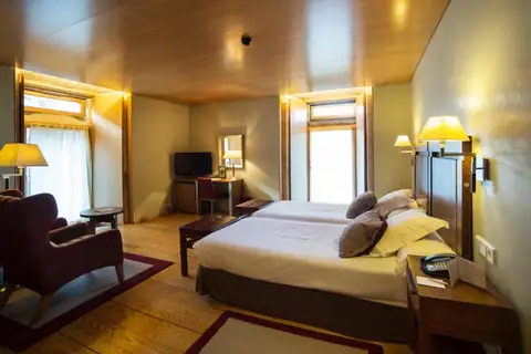 Habitación con dos camas, butaca y techo de madera en el Parador de Santo Estevo