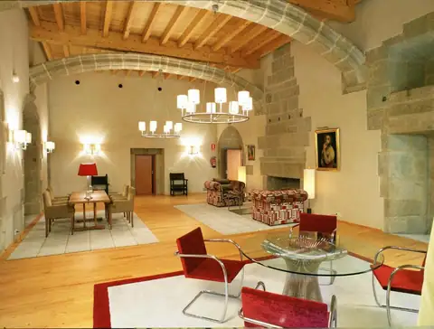 Salón noble con chimenea de piedra, techo de madera y butacas rojas en el Parador de Santo Estevo