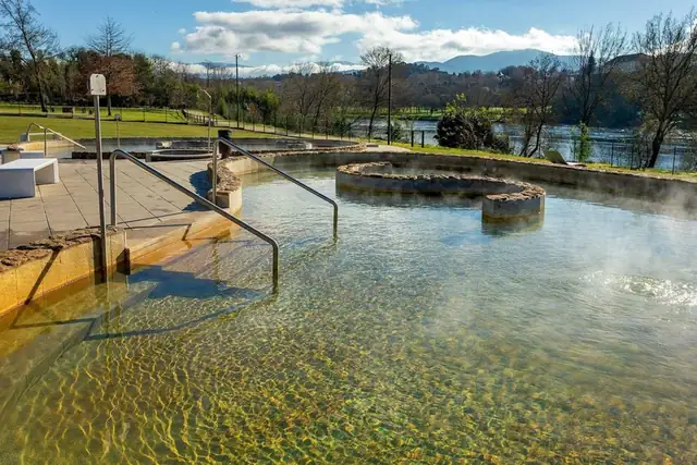 Piscina termal humeante con barandilla y muro de piedra junto al río Miño en el Espacio Termal de Teáns