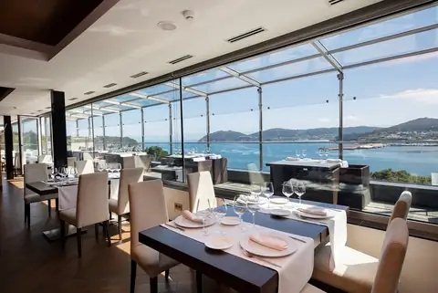 Restaurante con mesas preparadas y vistas panorámicas a la ría en el Hotel Thalasso Las Sirenas